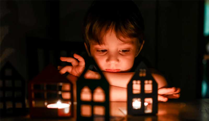 Criança observando pequenas casas iluminadas representando organização da rotina, vínculos familiares e impacto das decisões judiciais na vida infantil