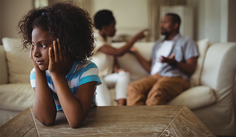 Criança triste em primeiro plano enquanto pais discutem ao fundo, representando o impacto emocional das decisões judiciais e conflitos familiares na infância