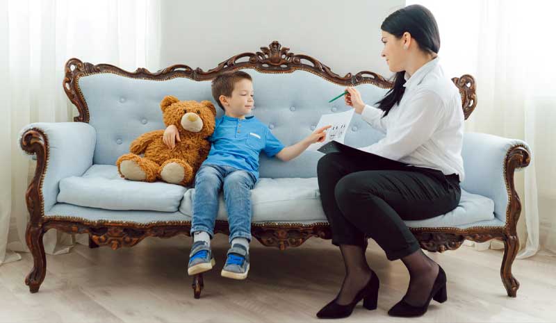 Garoto em atendimento com psicóloga, abraçando um urso de pelúcia enquanto observa uma folha com desenhos, representando psicologia infantil | Valente Perícias